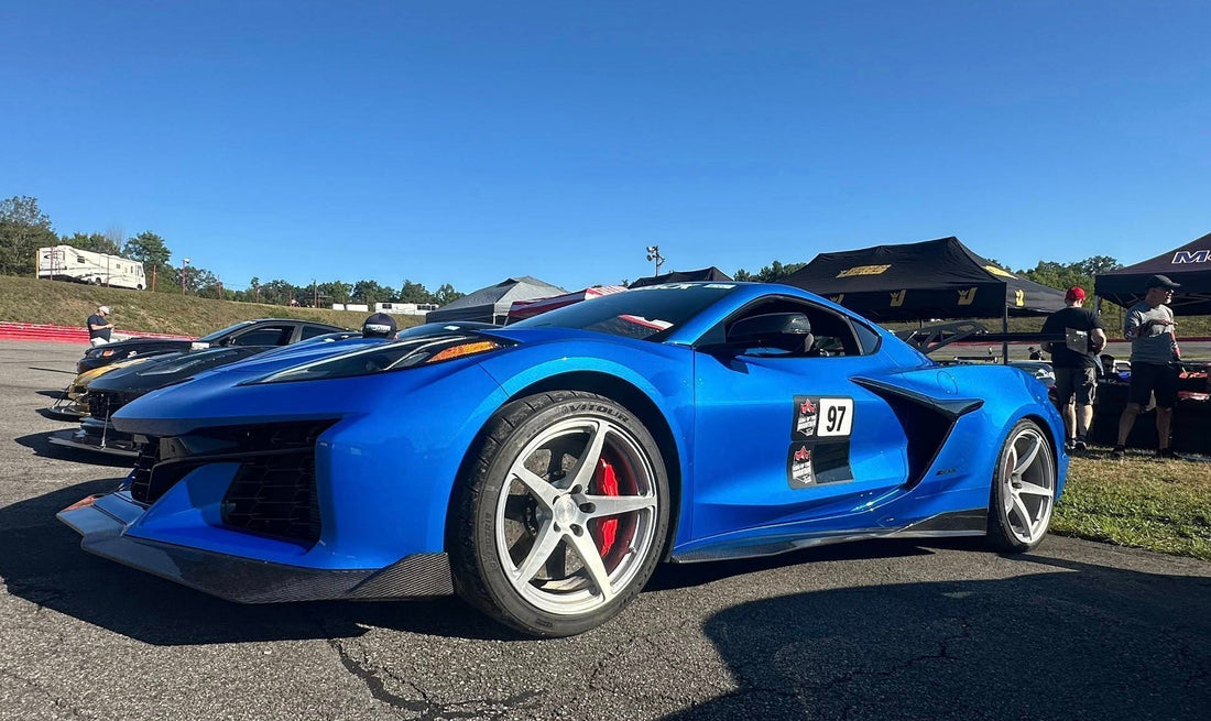 Angle from the front left of a blue C8 corvette with the background of an expansive blue sky